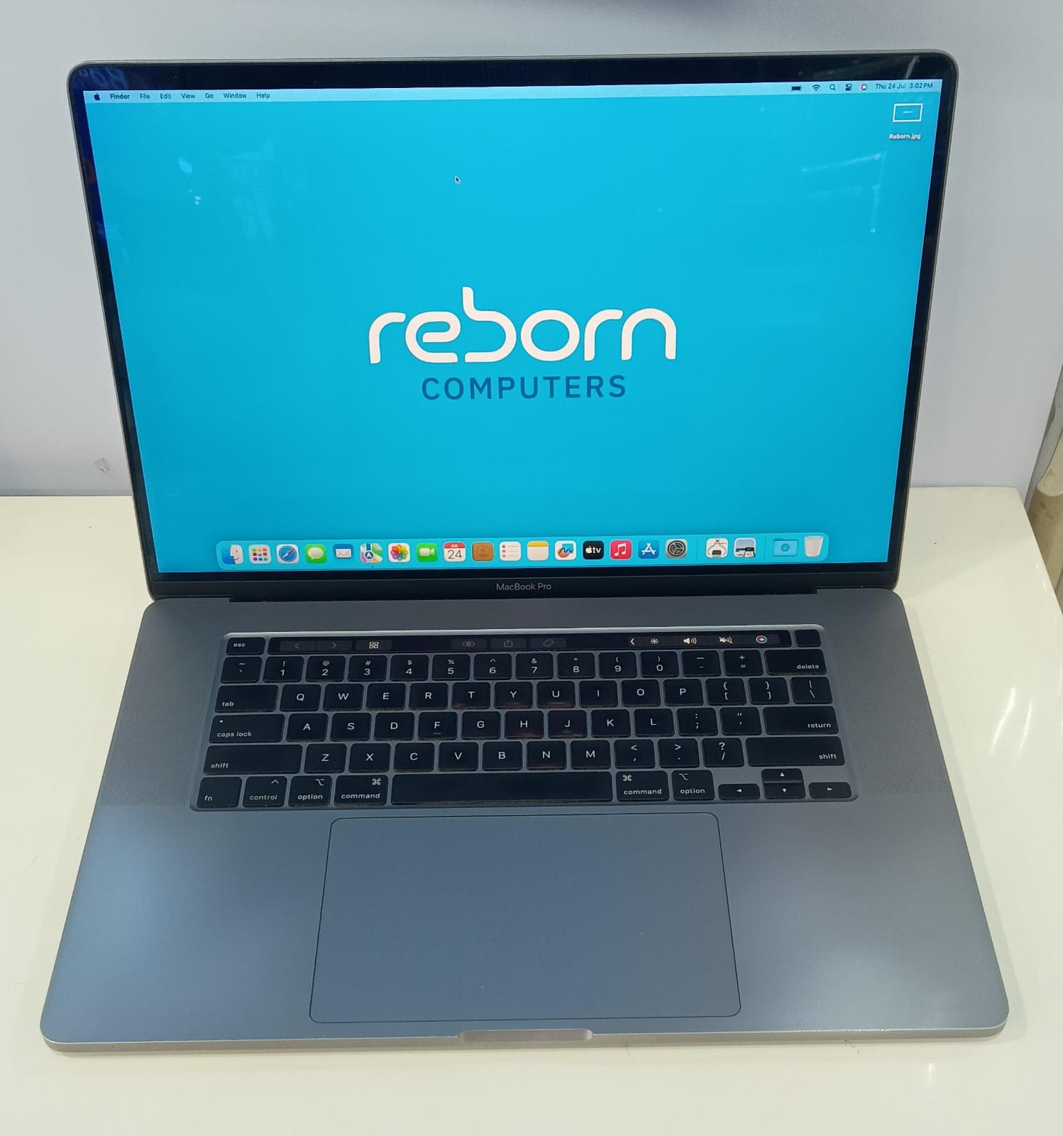 MacBook Pro 16-inch laptop in silver colour with touch bar. Wallpaper shows Reborn Computers logo in a blue background.